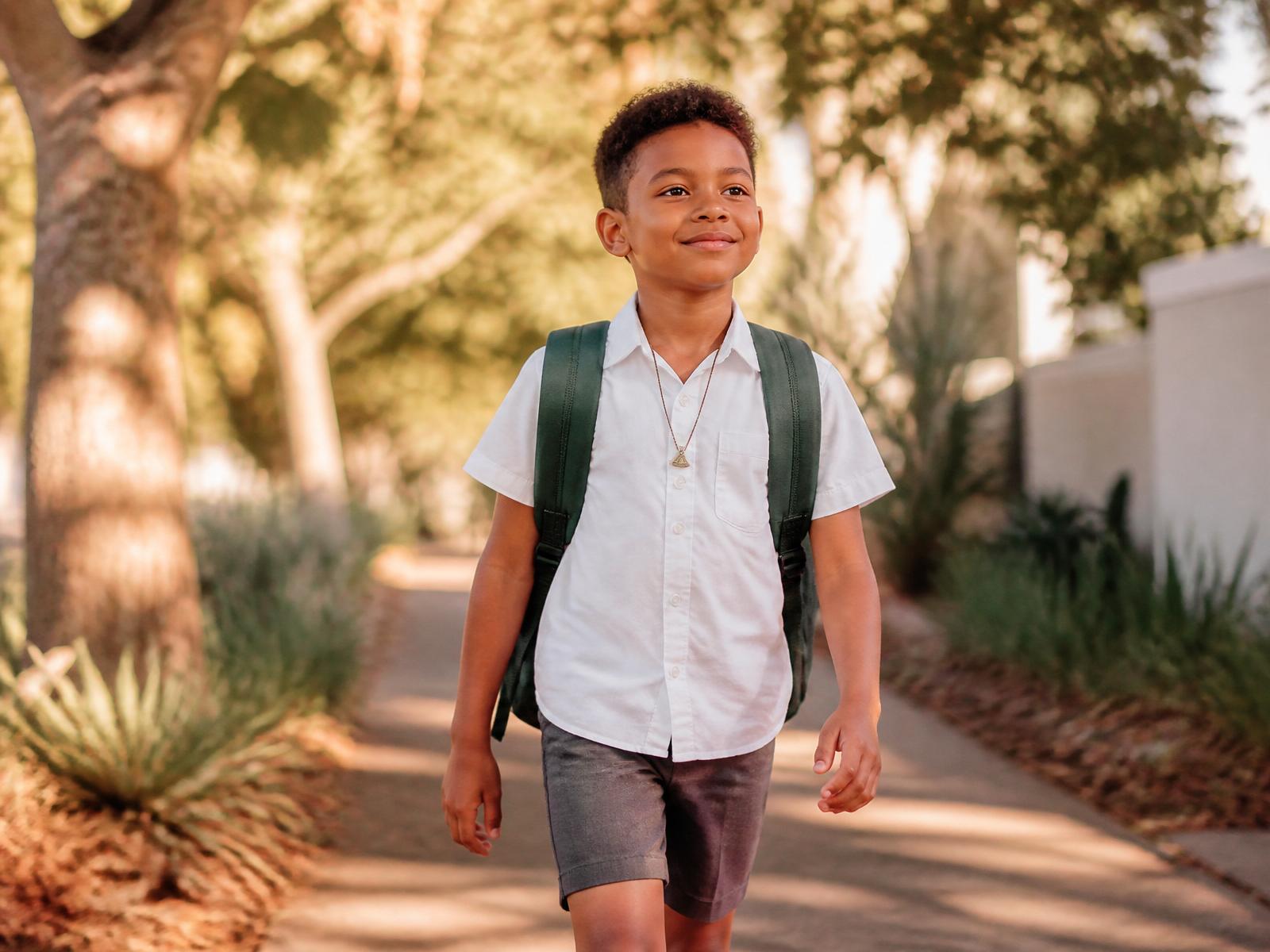 A young child walking confidently to school in warm morning light